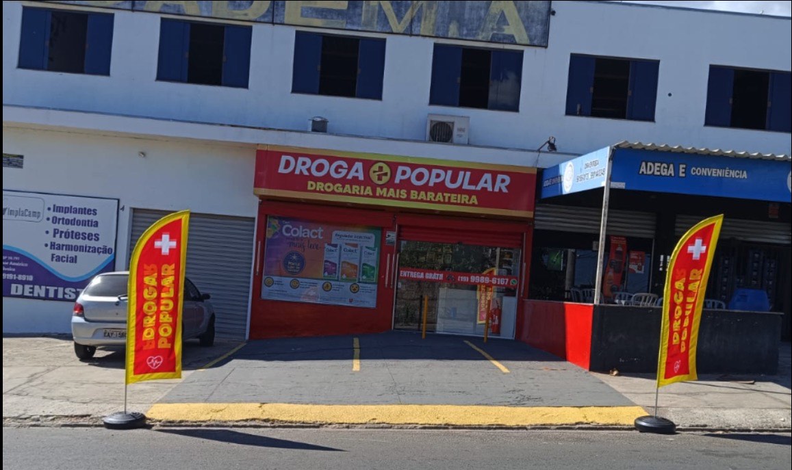 Fachada da Droga Popular na Avenida Dr. Eurídice José Bento, com letreiro vermelho e bandeiras na calçada